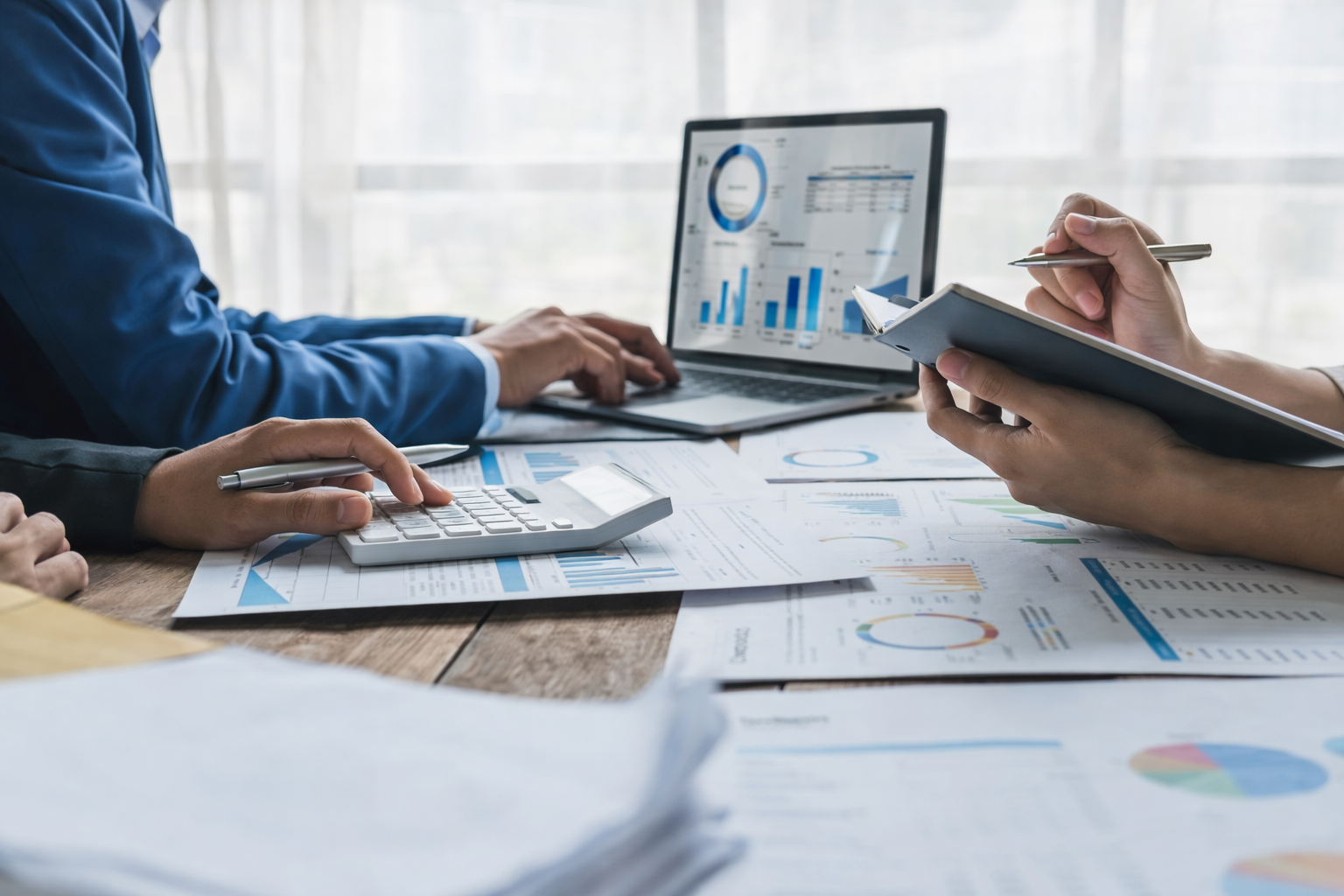 Two professionals reviewing financial reports with a calculator and laptop