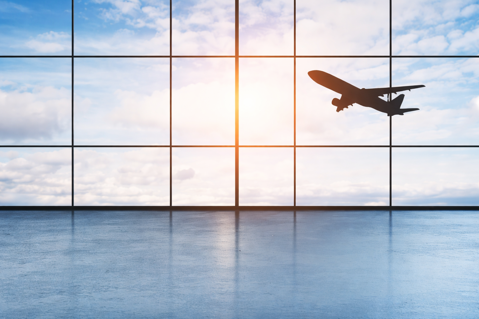Airplane taking off viewed through airport terminal windows at sunrise